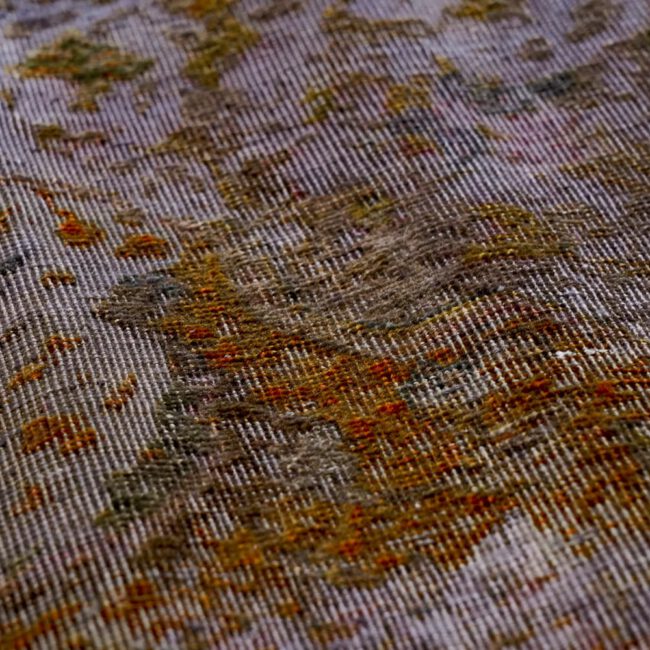 Close Up von einem Persian Art Design Teppich mit dunkel farbigem Muster auf grau aubergine farbenem Webgeflecht
